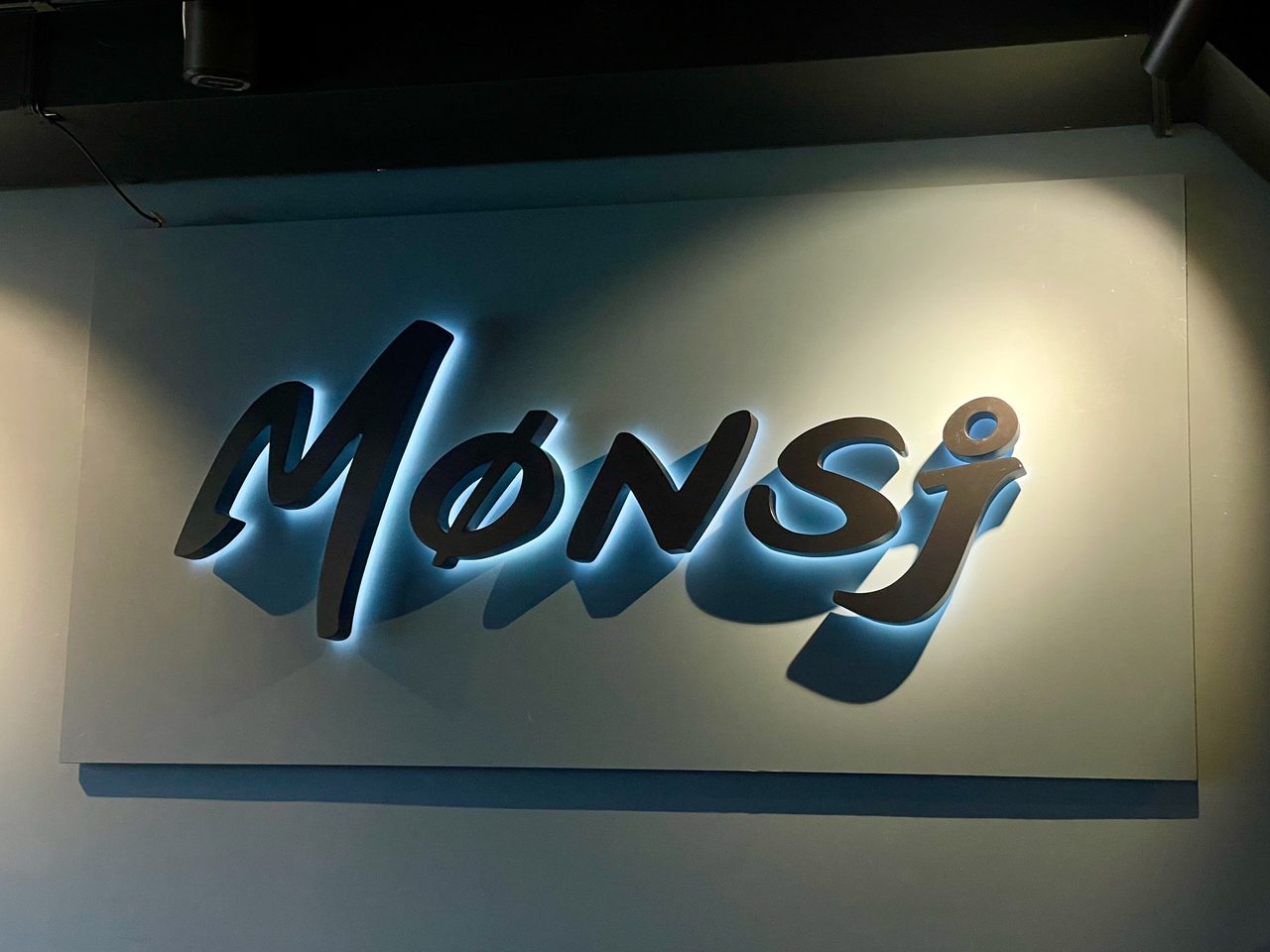 Mønsj Arendal restaurant logo inside the cozy waterfront restaurant in Arendal, Norway, with illuminated wall signage and atmospheric indoor lighting.