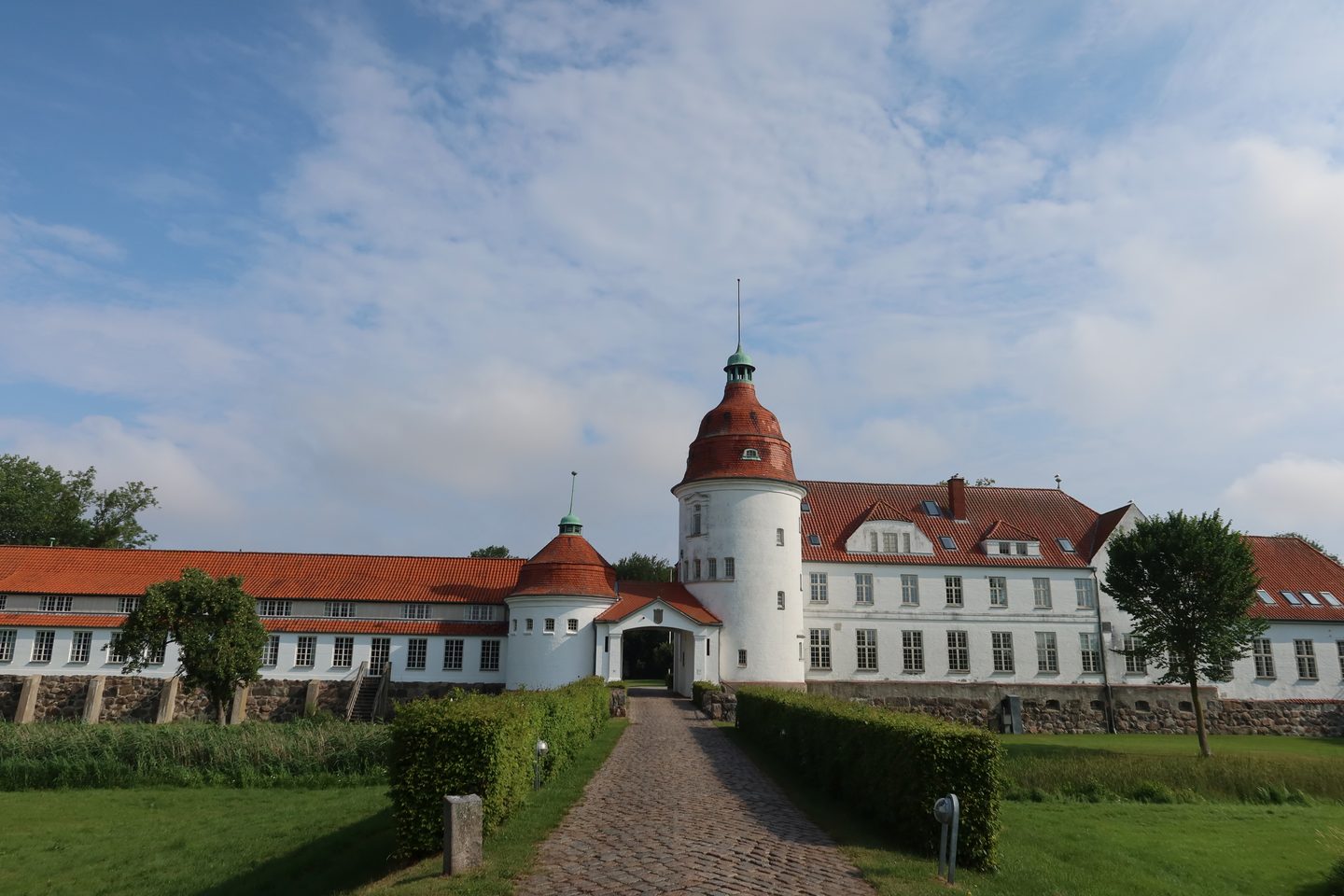 Nordborg Slot with white castle facade red tiled roofs cobblestone path and green garden in Nordborg Denmark