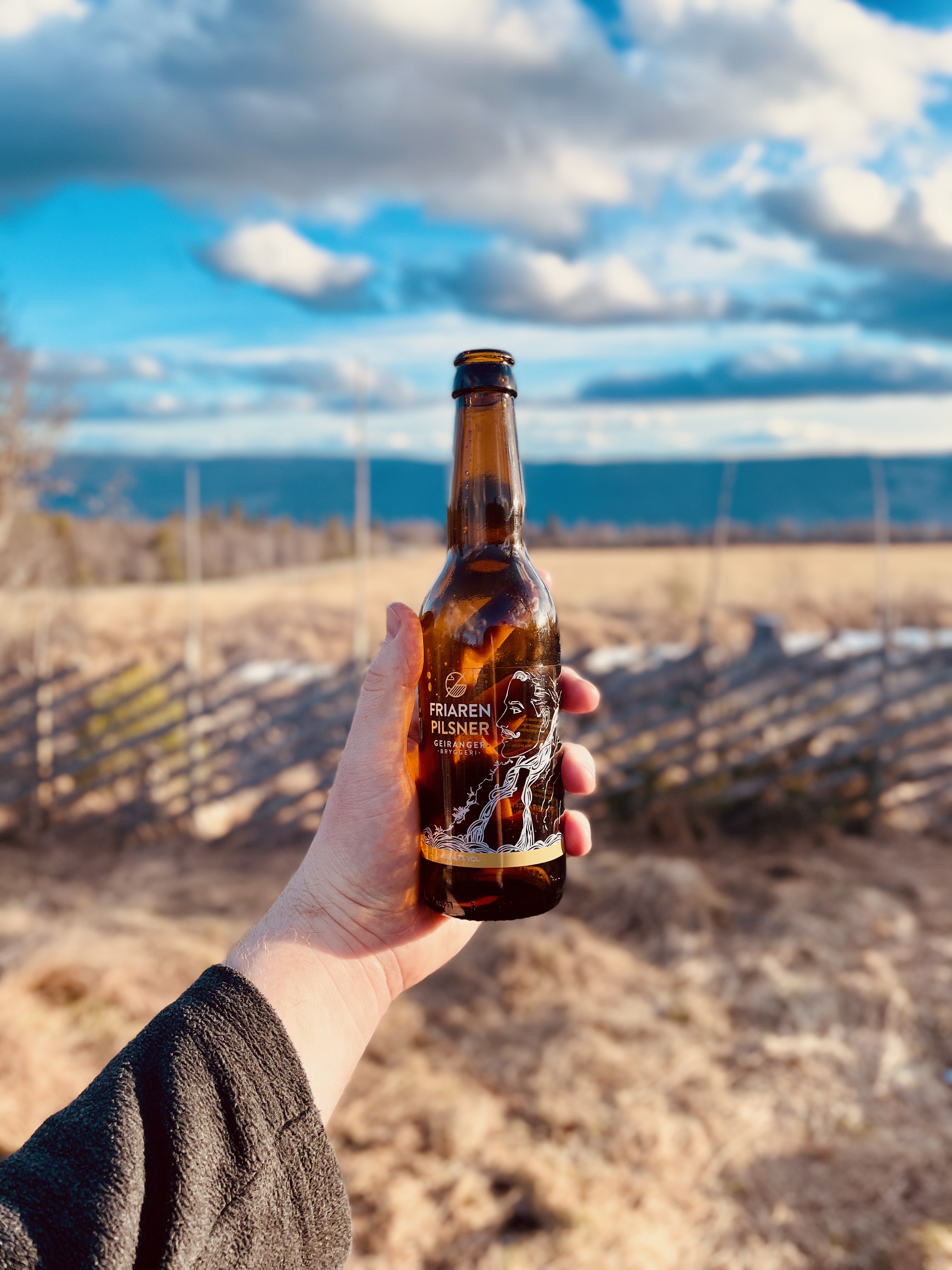 A can of Lom Bryggeri Ljos lager by the outdoor fire pit at Per’s stuggu Sør-Fron, with mountain views in the background.
