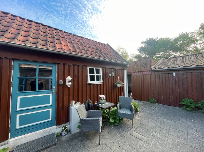 Private Annex Haderslev Review showing the cozy Airbnb courtyard in Haderslev with a blue door, wooden annex, outdoor chairs, small table, plants and red tiled roof.
