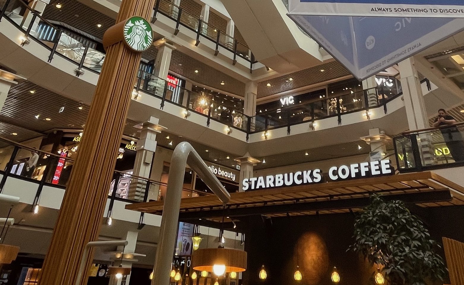 Starbucks Oslo City Review, wide view of Oslo City shopping mall atrium with Starbucks Coffee below, glass ceiling, hanging mall banner, multiple floors and surrounding stores in central Oslo