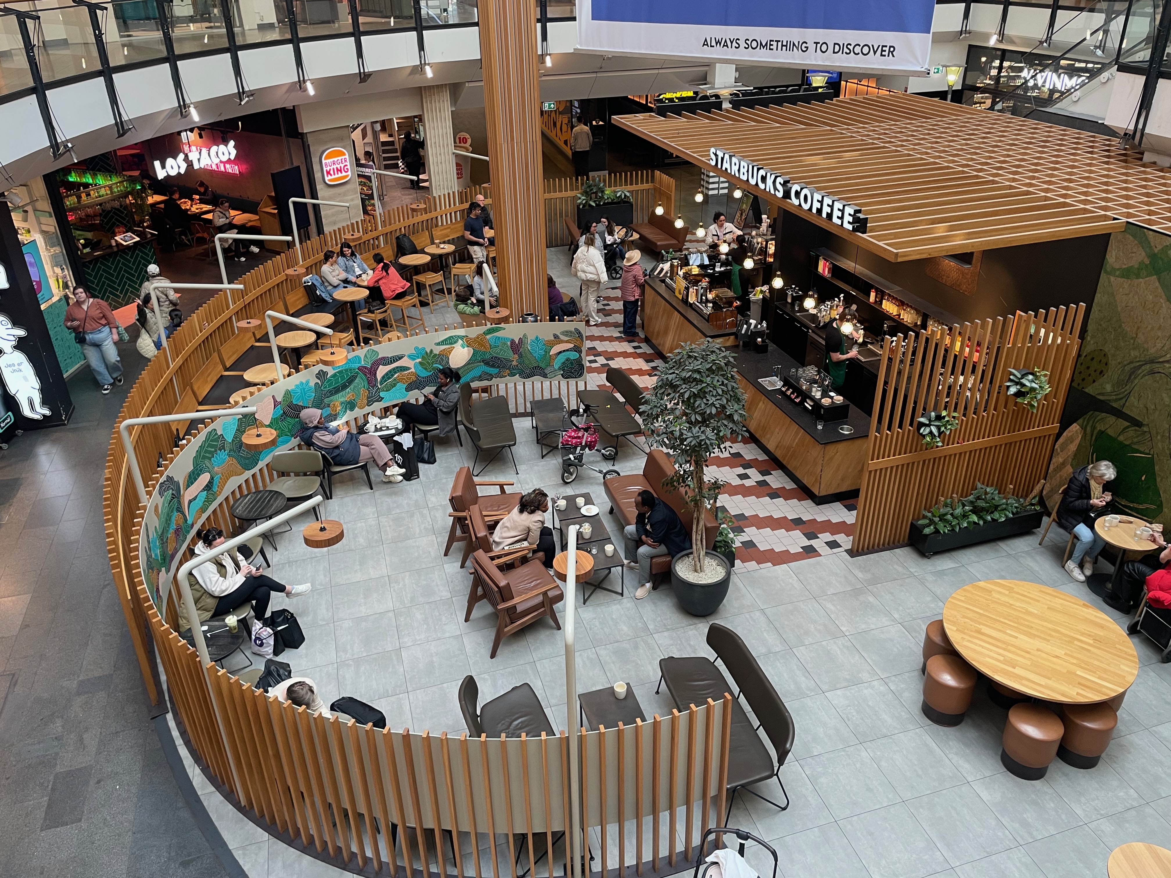 Starbucks Oslo City Review, overhead view of the Starbucks seating area inside Oslo City shopping mall with wooden dividers, café tables, plants, Burger King and Los Tacos nearby